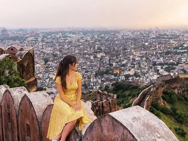 Eine Frau in einem gelben Kleid sitzt auf einer Festungsmauer mit Blick auf die Stadt.
