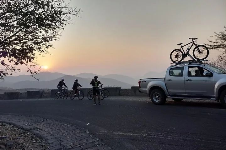 Cyclists gather near a pickup truck with bikes during a beautiful sunrise.