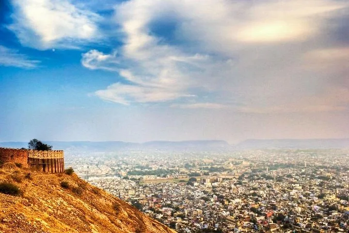 A fortified hill overlooks a sprawling city beneath a dramatic cloudy sky.