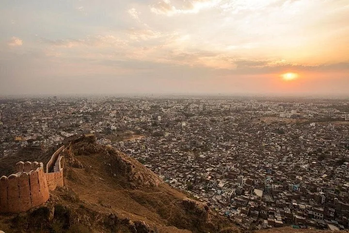 El sol se pone sobre una vasta ciudad densamente poblada, vista desde la muralla de un fuerte.